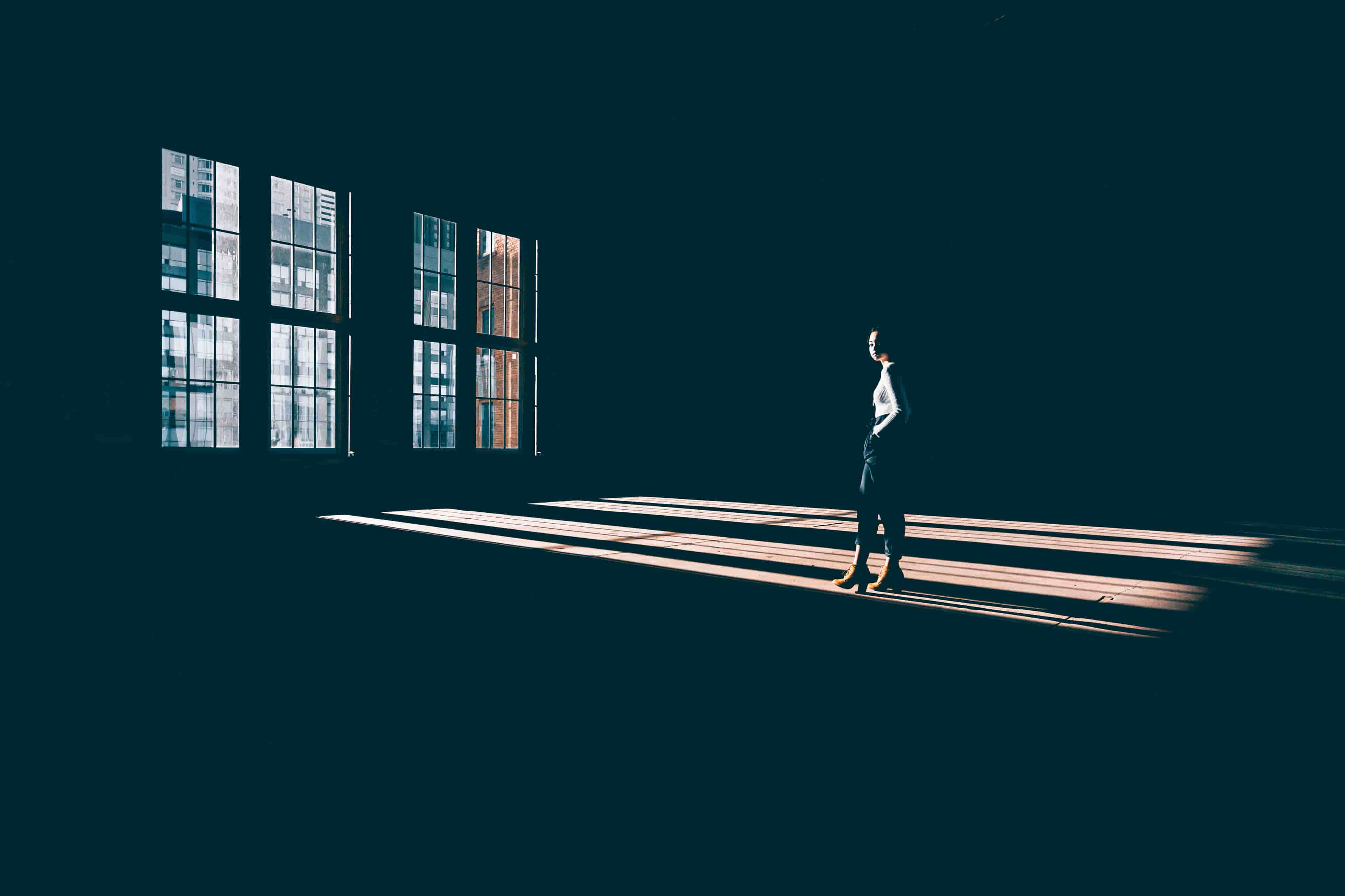 Female model standing in a dark room being highlighted from sunshine coming through the window. Extreme juxtaposition.