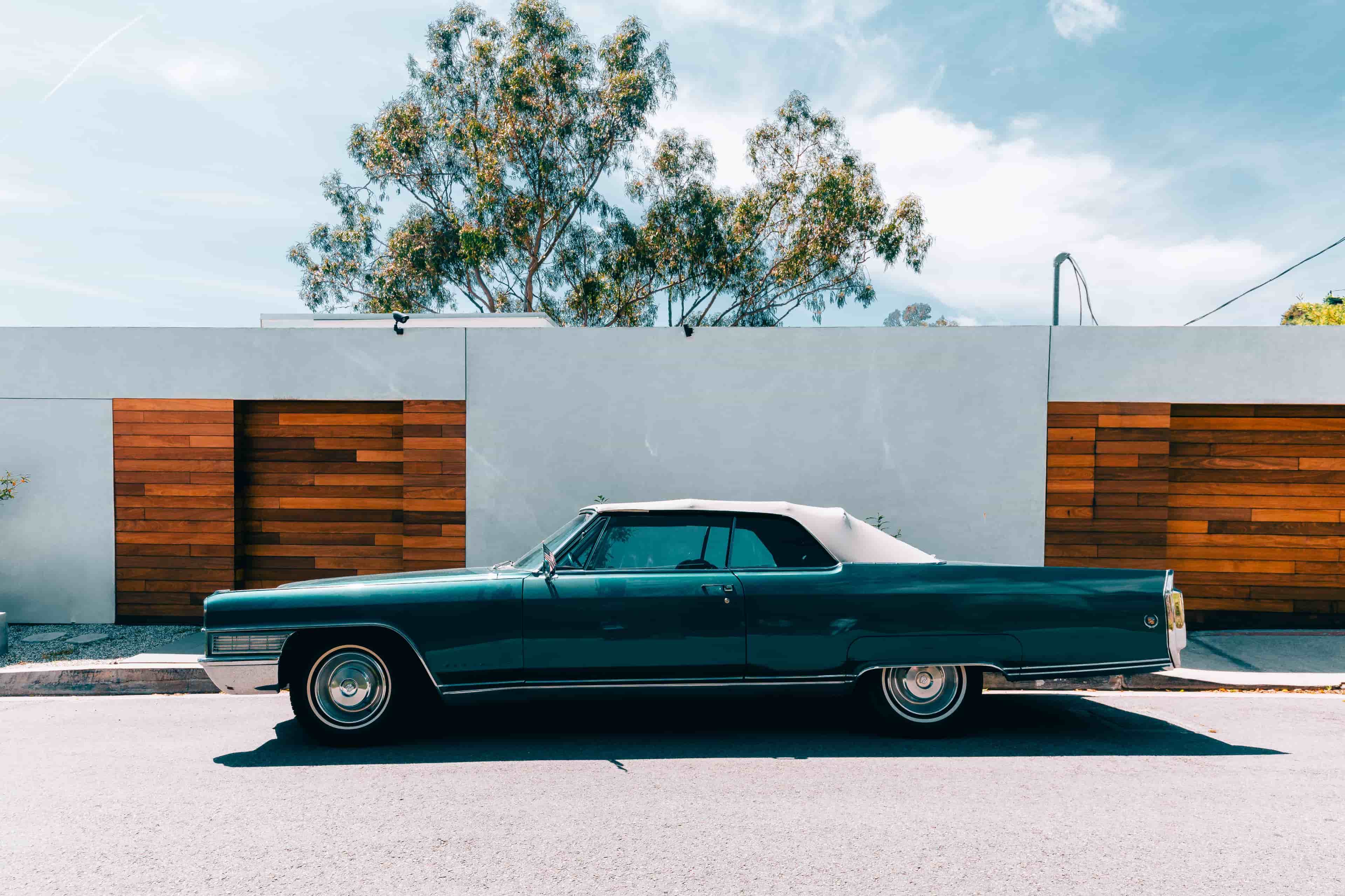 An old school Cadillac parked in front of a driveway in Los Angeles with blue skies and a tree in the background