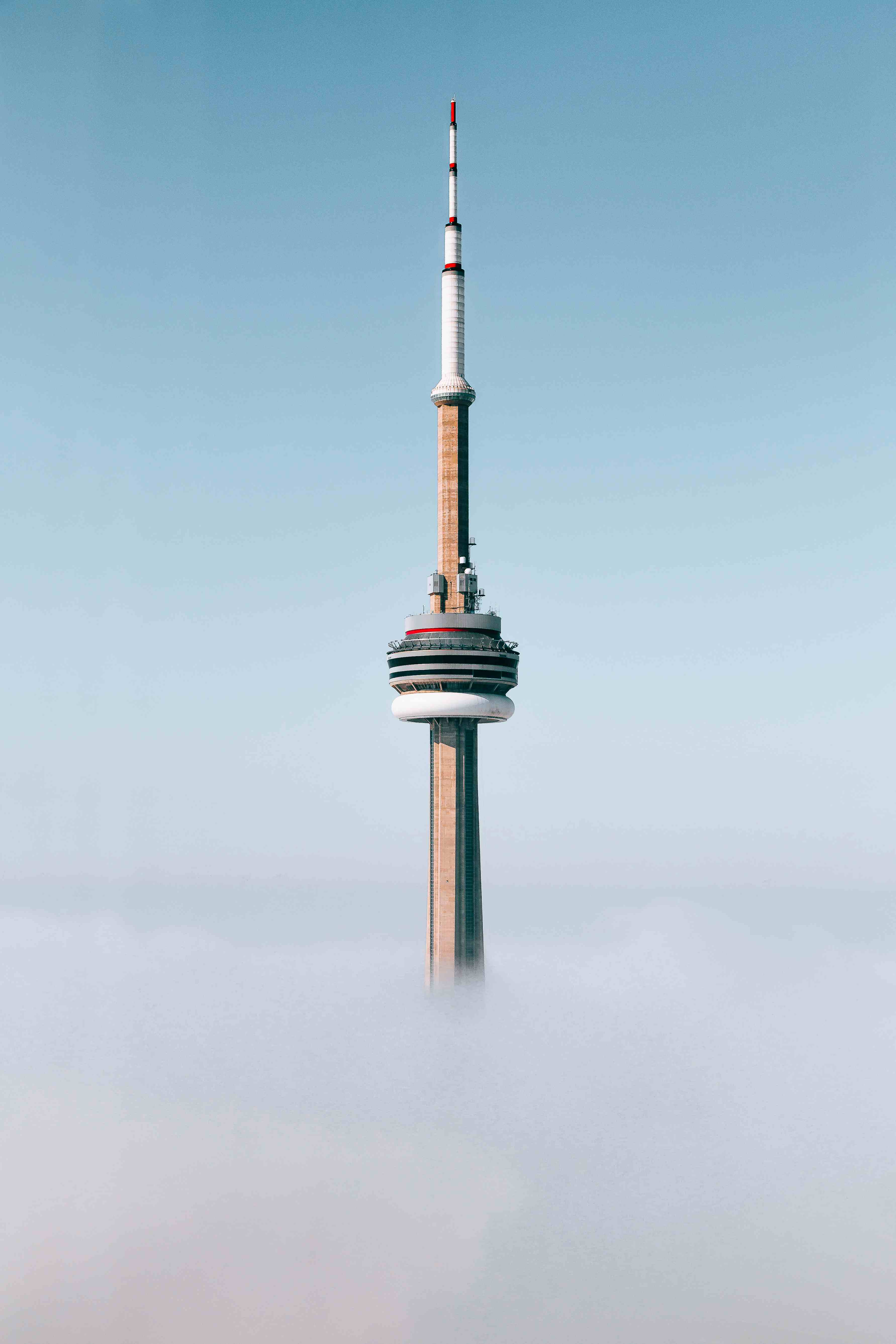 A photo of the top of half of the CN Tower in Toronto, Canada, standing tall above the clouds with a blue sky