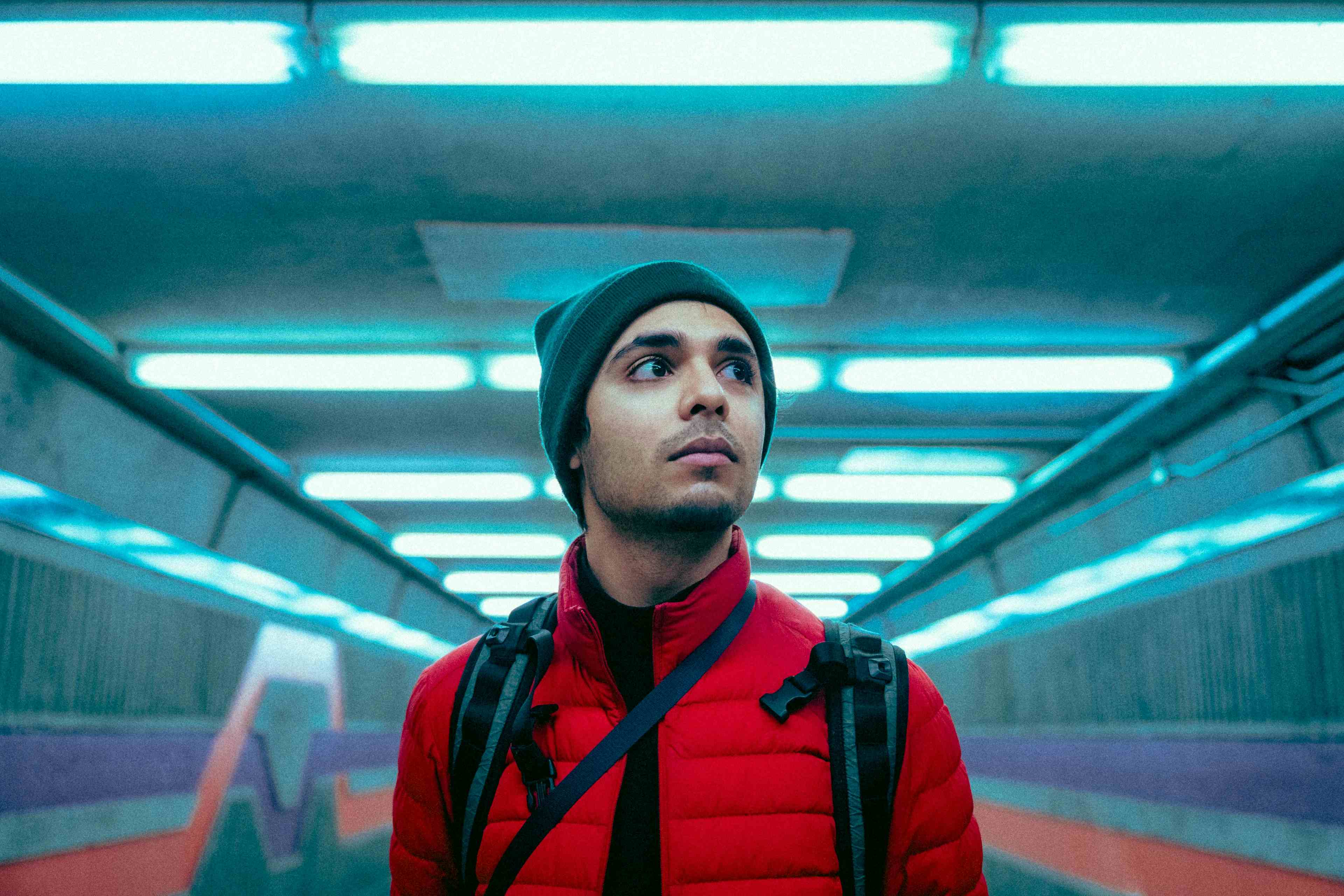 A futuristic, cinematic photo of myself standing in front of blue tinted lights in the Montreal metro, wearing a red jacket