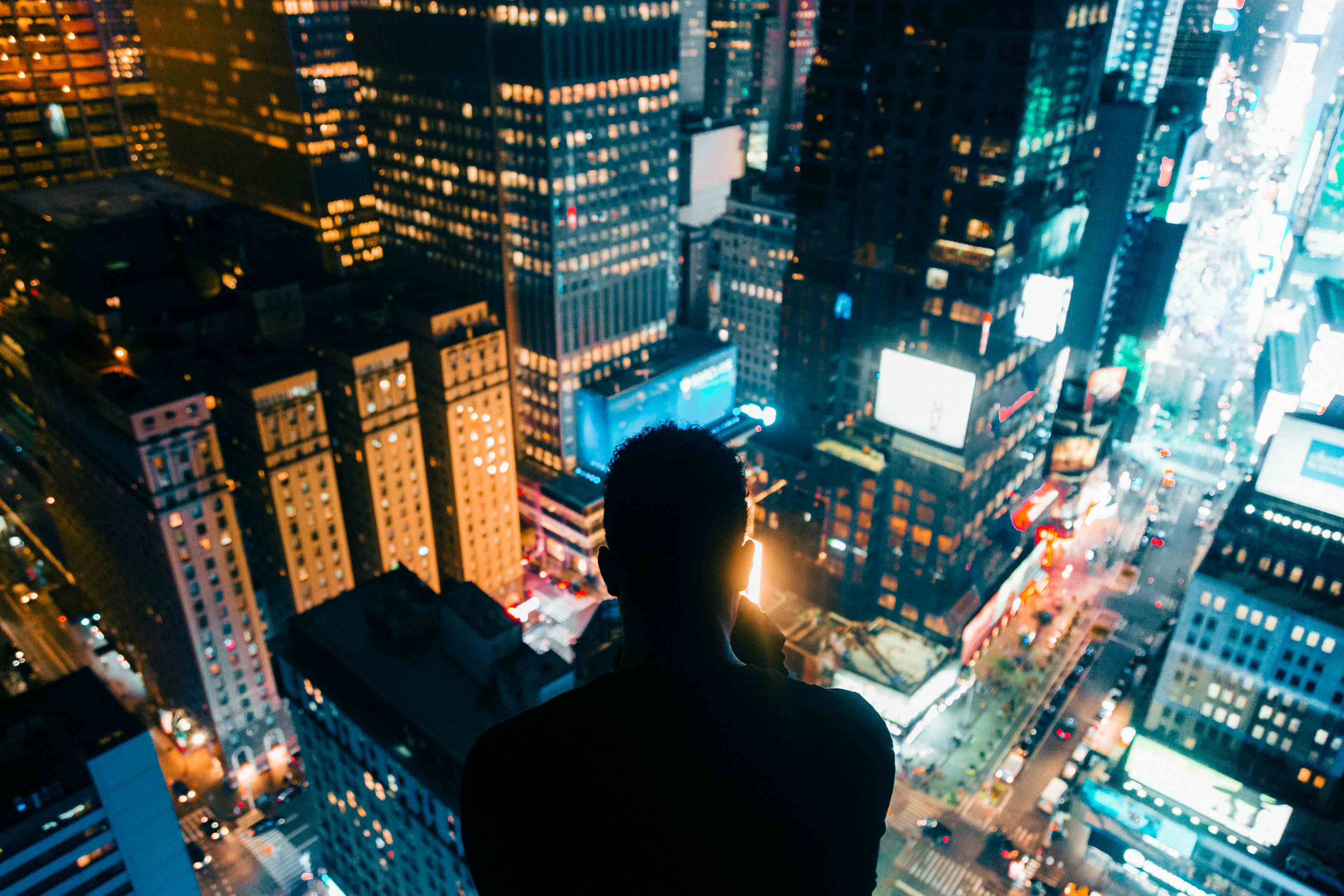 A man sitting on top of a building looking down and taking a photo of New York City's Times Square at night